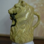 Broc barbotine Lion tenant un lézard dans sa gueule. Fond ocre. Hauteur 20cms