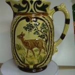 Broc barbotine décor forêt un cerf sur le recto et une biche sur l'autre face. fond ocre. hauteur 20,5 cms.